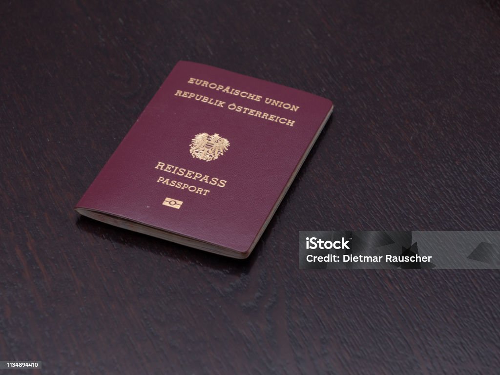 Red European passport of Austrian nationality on a wooden table.